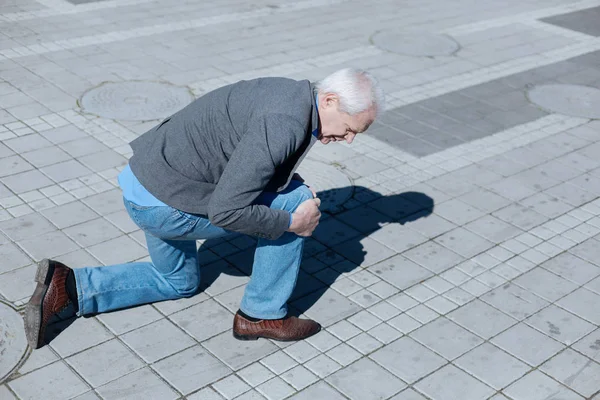 Aged pensioner falling on the ground in the street