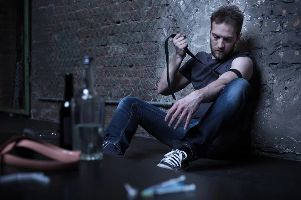 Apathetic addict tying tourniquet in the dark basement — Stock Photo, Image