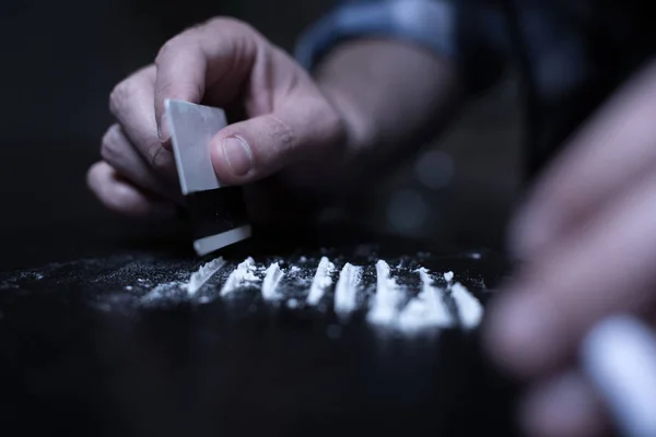 Опытный наркоман готовит кокаиновые линии в темном месте — стоковое фото