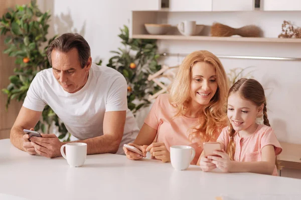 Familia positiva calificada usando teléfonos inteligentes en casa — Foto de Stock
