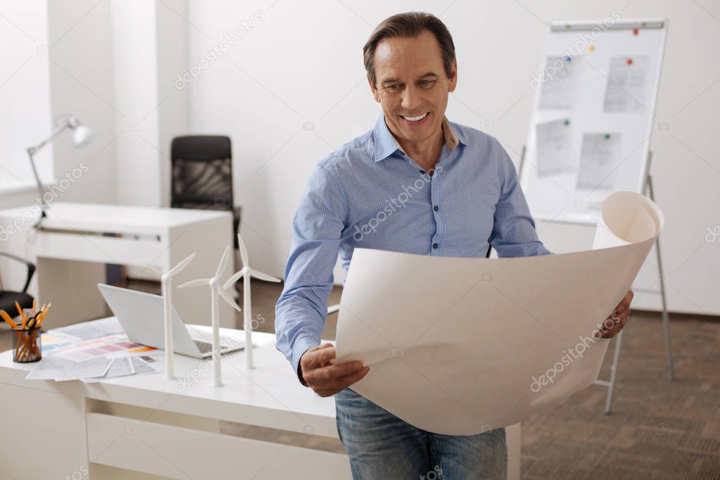 Cheerful engineer holding blueprint in the office