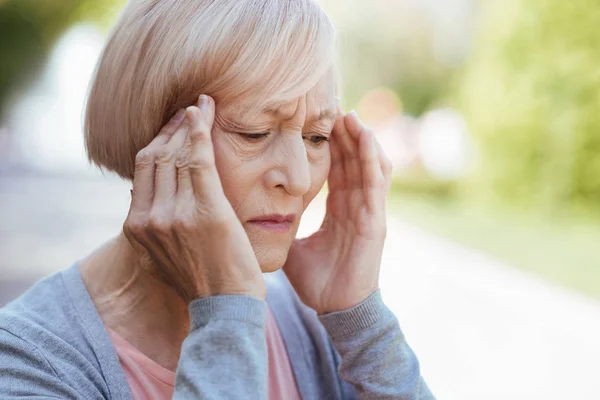 Koncentrovaná důchodce, trpící bolesti hlavy na ulici — Stock fotografie