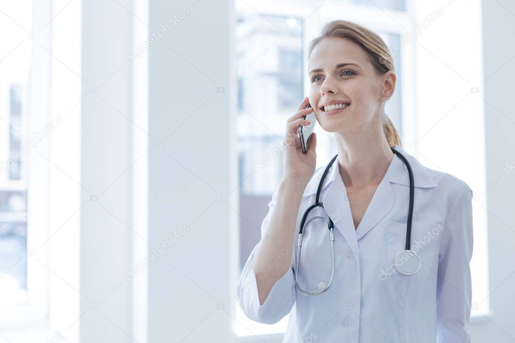 Happy young doctor using phone in the hospital