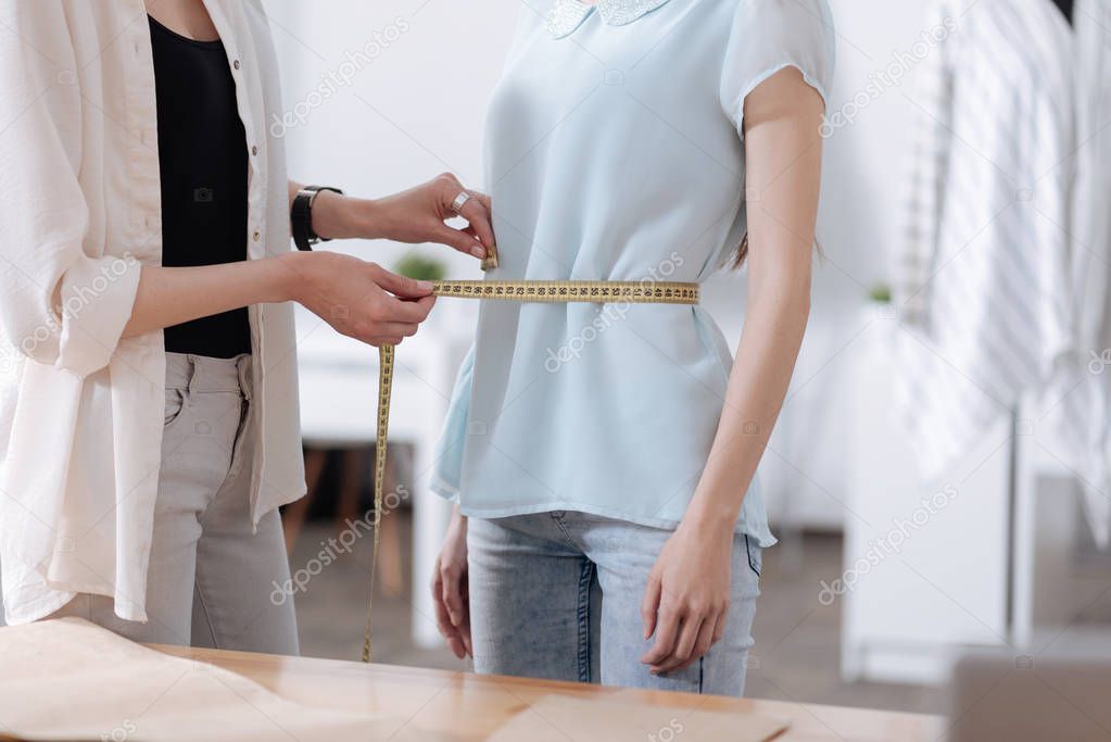 Slim woman measuring the waist of her colleague
