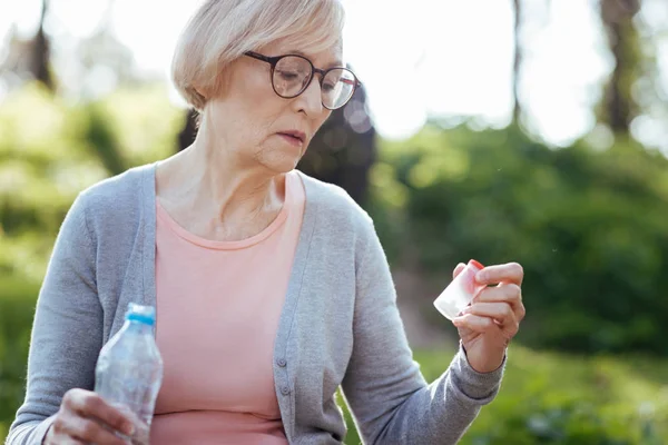 Inblandade gamla kvinna med flaska med piller i parken — Stockfoto