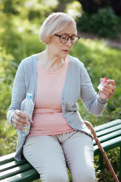 Envejecimiento concentrado mujer sosteniendo botella con pastillas al aire libre — Foto de Stock