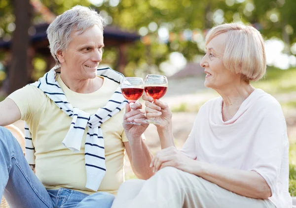 Усміхнена старша пара п'є вино в парку — стокове фото