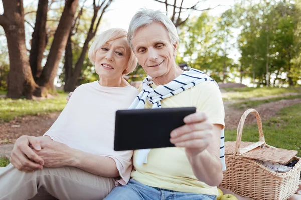 Pareja mayor calificada usando dispositivo electrónico en el parque —  Fotos de Stock