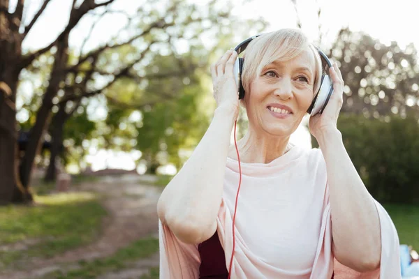 Cheerful aging woman enjoying music in headphones outdoors — Stock Photo, Image