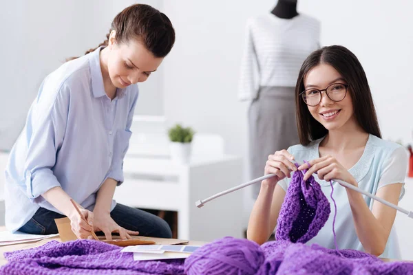 Vrolijke jonge kleermaker genieten van haar breiwerk — Stockfoto