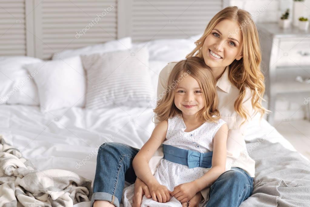 Happy smiling mother and daughter hugging on bed