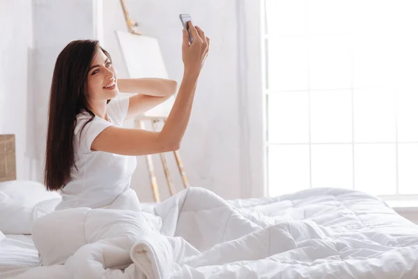 Unga brunett tar selfie i sängen. — Stockfoto