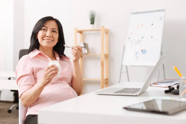 Grávida positiva mulher comendo jogurt no escritório — Fotografia de Stock