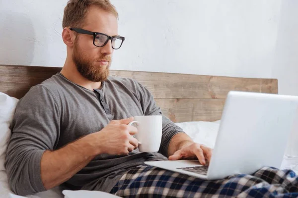 Handsome bearded man working with laptop in bed — Stock Photo, Image