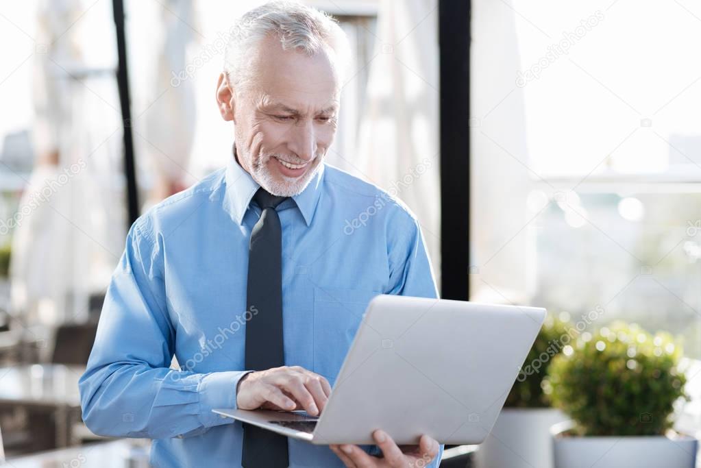 Positive delighted male person using his laptop