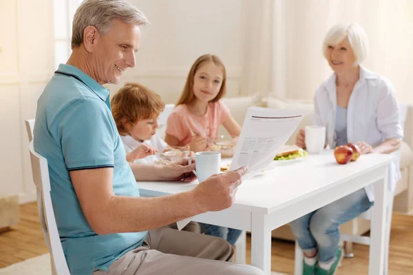 Abuelo inteligente positivo leyendo un periódico durante el desayuno —  Fotos de Stock