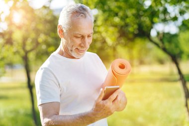 Parkta akıllı telefon kullanan olumlu sportif emekli adam