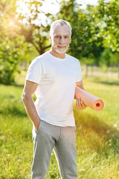 Позитивный пожилой человек держит коврик для йоги — стоковое фото