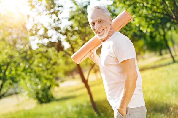 Cheerful aged man holding roll mat on the shoulder — Stock Photo, Image