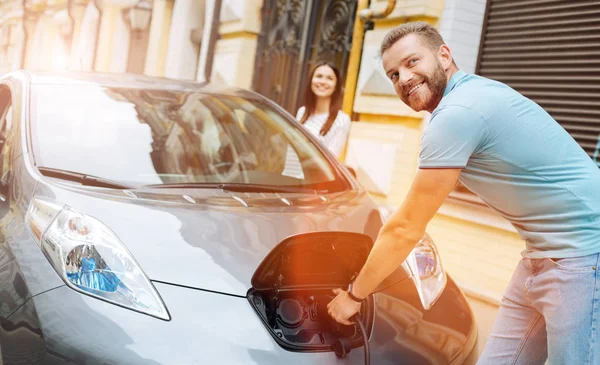Усміхнений чоловік від'єднує зарядний пристрій від машини — стокове фото