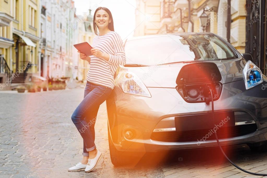 Young woman using tablet while charging the car