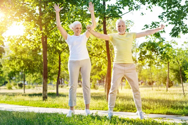 Overjoed coppia anziana facendo esercizi sportivi nel parco — Foto Stock