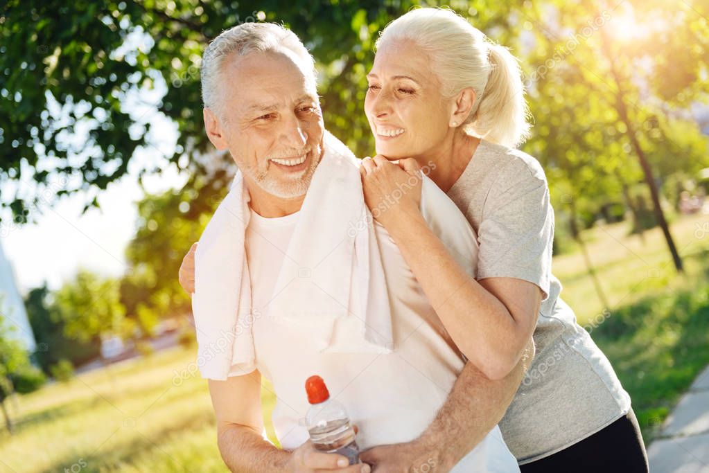 Positive retired smiling couple resting in the park after jogging