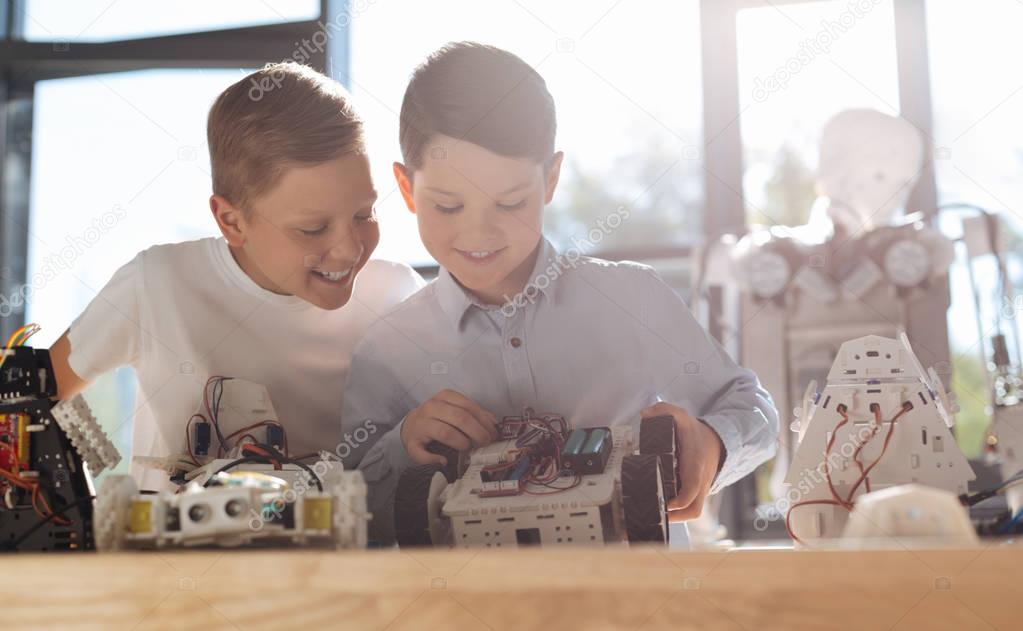 Smiling boy watching his friend construct a robot car