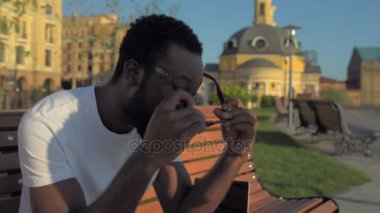 Parlak genç adam bankta otururken gözlüklerini koyarak