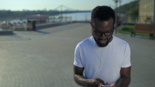 Giovane ragazzo positivo che cammina e ascolta musica — Video Stock