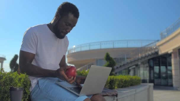 Chico trabajando en el ordenador portátil y tirar manzana — Vídeos de Stock