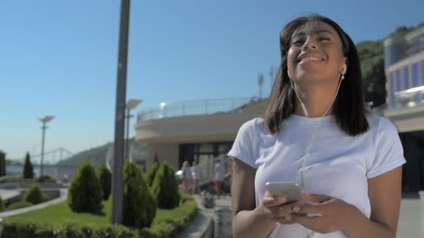 Beaming menina afro-americana andando com fones de ouvido — Vídeo de Stock