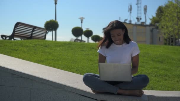 Позитивная юная леди работает в парке со скрещенными ногами — стоковое видео
