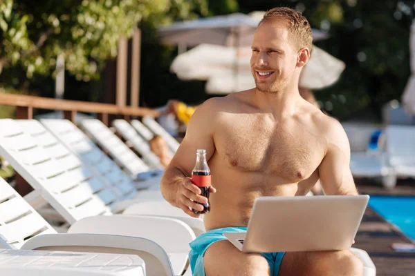 Upbeat man having fizzy drink while working near pool — Stock Photo, Image