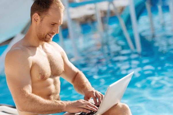 Shirtless man working on the laptop near a swimming pool — Stock Photo, Image