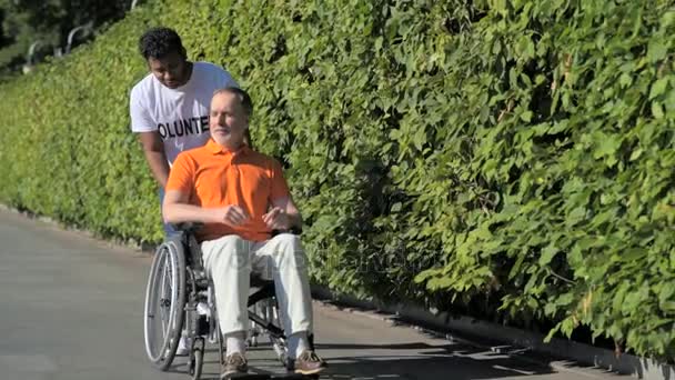 Voluntario hindú útil caminando con un hombre con silla de ruedas — Vídeo de stock