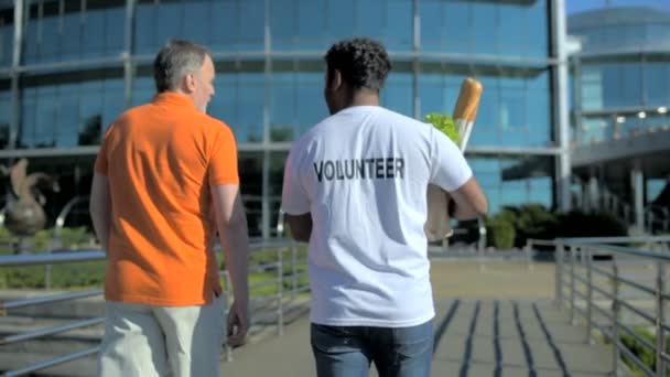 Bakifrån av en aktiv volontär att hjälpa en äldre man — Stockvideo
