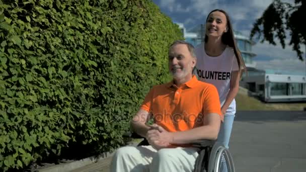 Sukarelawan wanita Positif mendorong pria berkursi roda — Stok Video