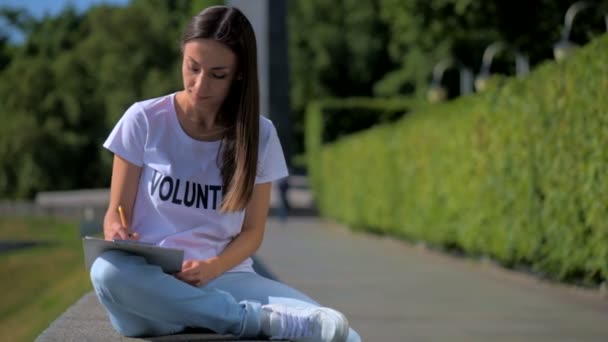 Сконцентрированная женщина-волонтер делает заметки на открытом воздухе — стоковое видео