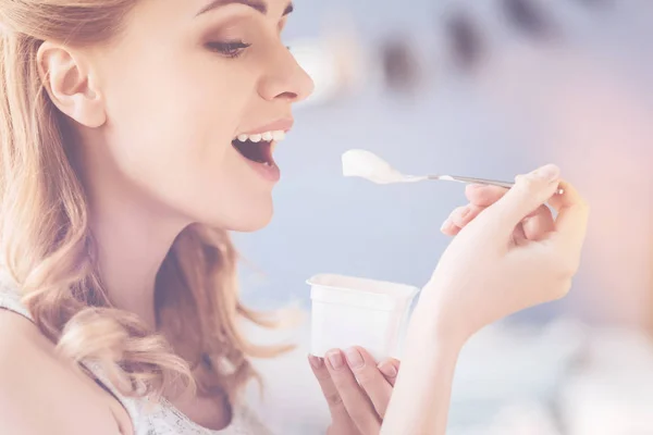 Pleasant delighted woman eating yoghurt
