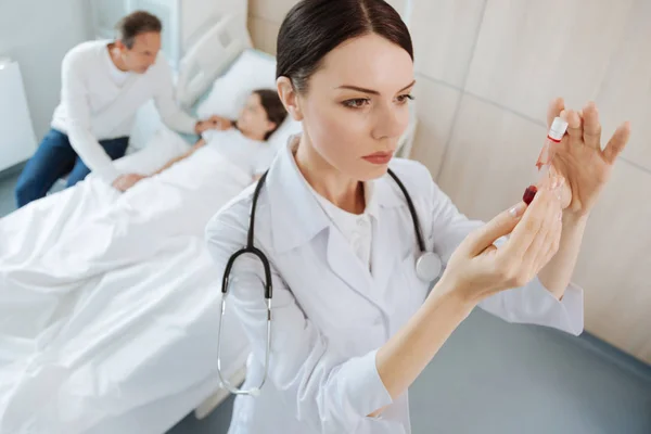 Seriöser, kluger Arzt, der mit Blut ins Reagenzglas schaut — Stockfoto