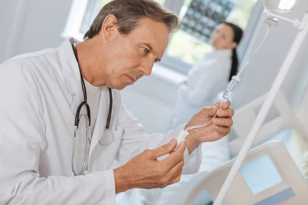 Médico sério e atencioso segurando um tubo IV — Fotografia de Stock