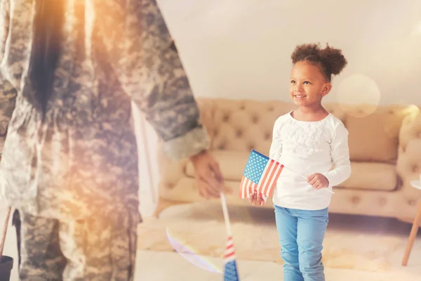 Niña de pie frente a su madre con bandera americana — Foto de Stock