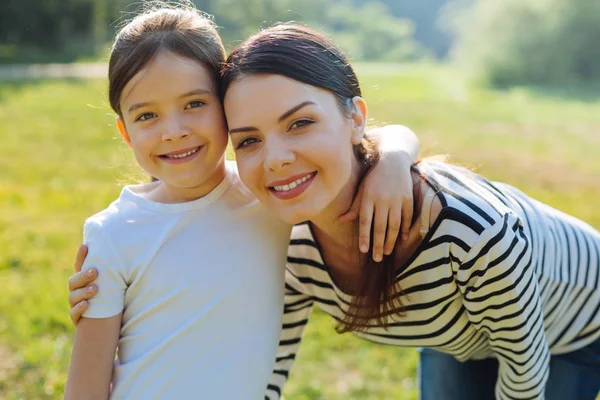 Pleasant cheerful daughter and mother smiling at the camera — Stock Photo, Image