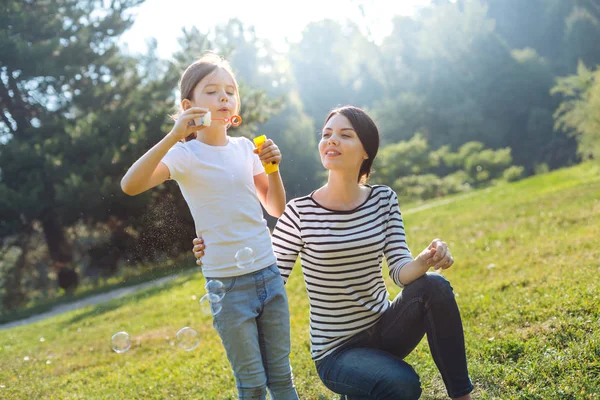 Madre cariñosa viendo a su hija jugar con burbujas de jabón — Foto de Stock