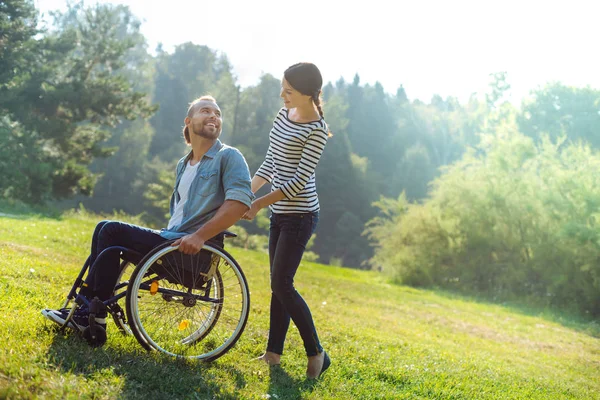 Fürsorgliche Ehefrau trägt ihren behinderten Mann im Rollstuhl — Stockfoto