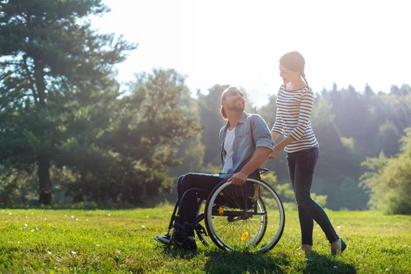 Femme souriante portant fauteuil roulant de son mari handicapé — Photo