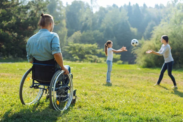 Homme à mobilité réduite regardant sa famille jouer avec le ballon — Photo