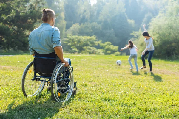 Homme en fauteuil roulant regardant sa famille jouer au football — Photo