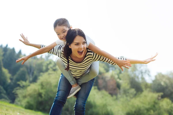 Mãe alegre dando um piggyback para sua filhinha — Fotografia de Stock